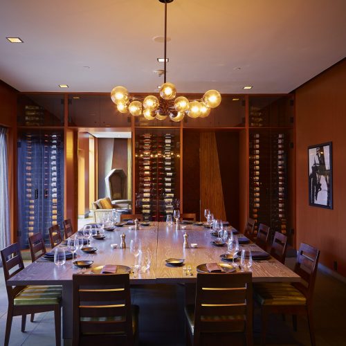 A private dining table at The Reserve with a large wooden table with seating around, a wine rack on the entrance wall with the table set for Brunch at Highland Dallas, TX