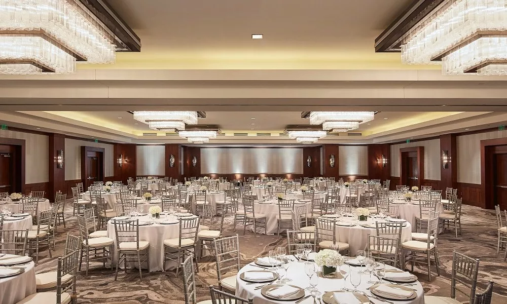 The ballroom at Highland Dallas set for a wedding with white linen tables, silver ballroom chairs and white floral arrangements in Dallas, TX