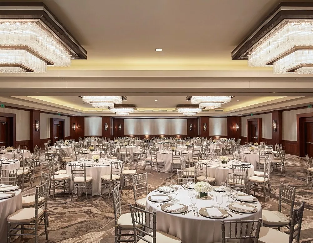The ballroom at Highland Dallas set for a wedding with white linen tables, silver ballroom chairs and white floral arrangements in Dallas, TX