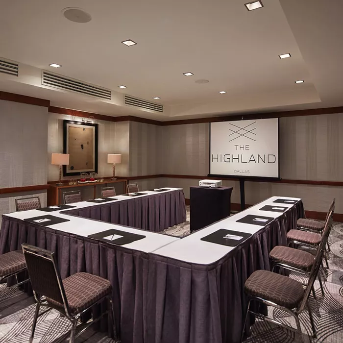Fresco meeting room set for a meeting with white and dark purple linens and meeting chairs around a 'u' shaped table with a projector projecting the Highland Dallas, TX logo