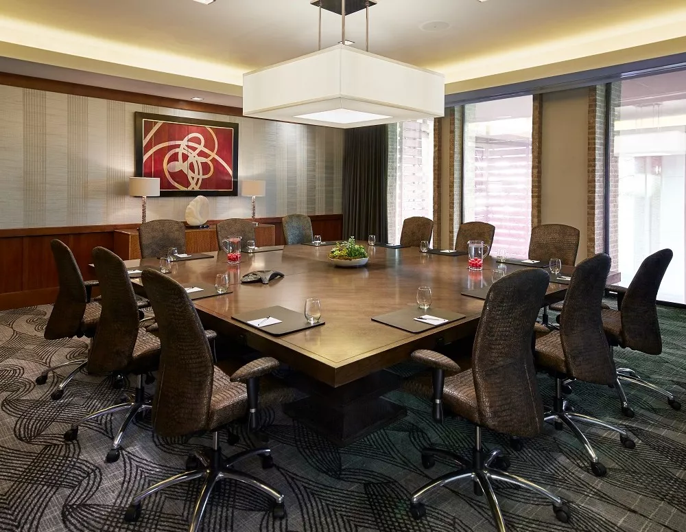Maestro meeting room at Highland Dallas with a large square wooden meeting table and office chairs surrounding and large floor to ceiling windows in Dallas, TX