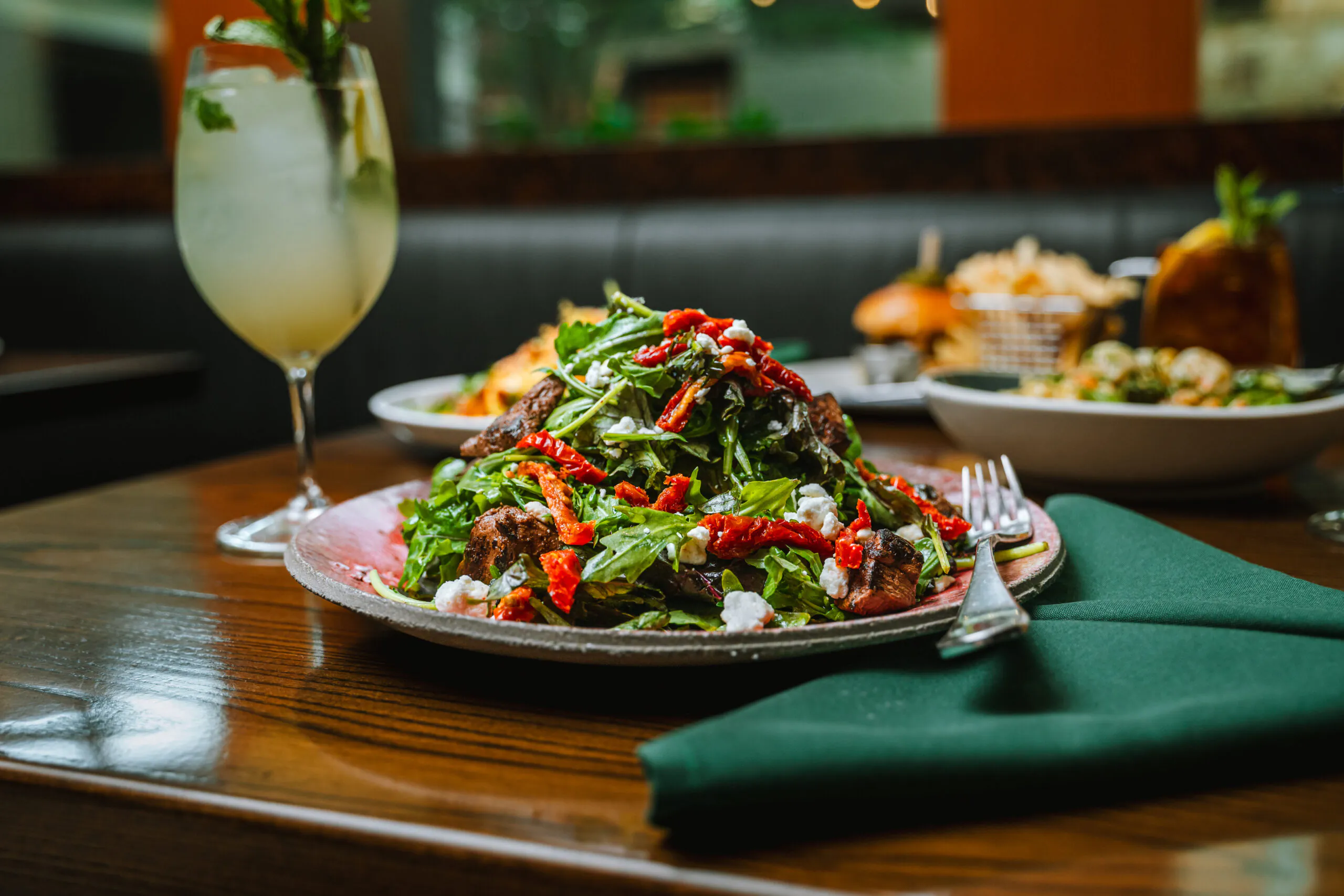 table with a vibrant salad and cocktail in the background