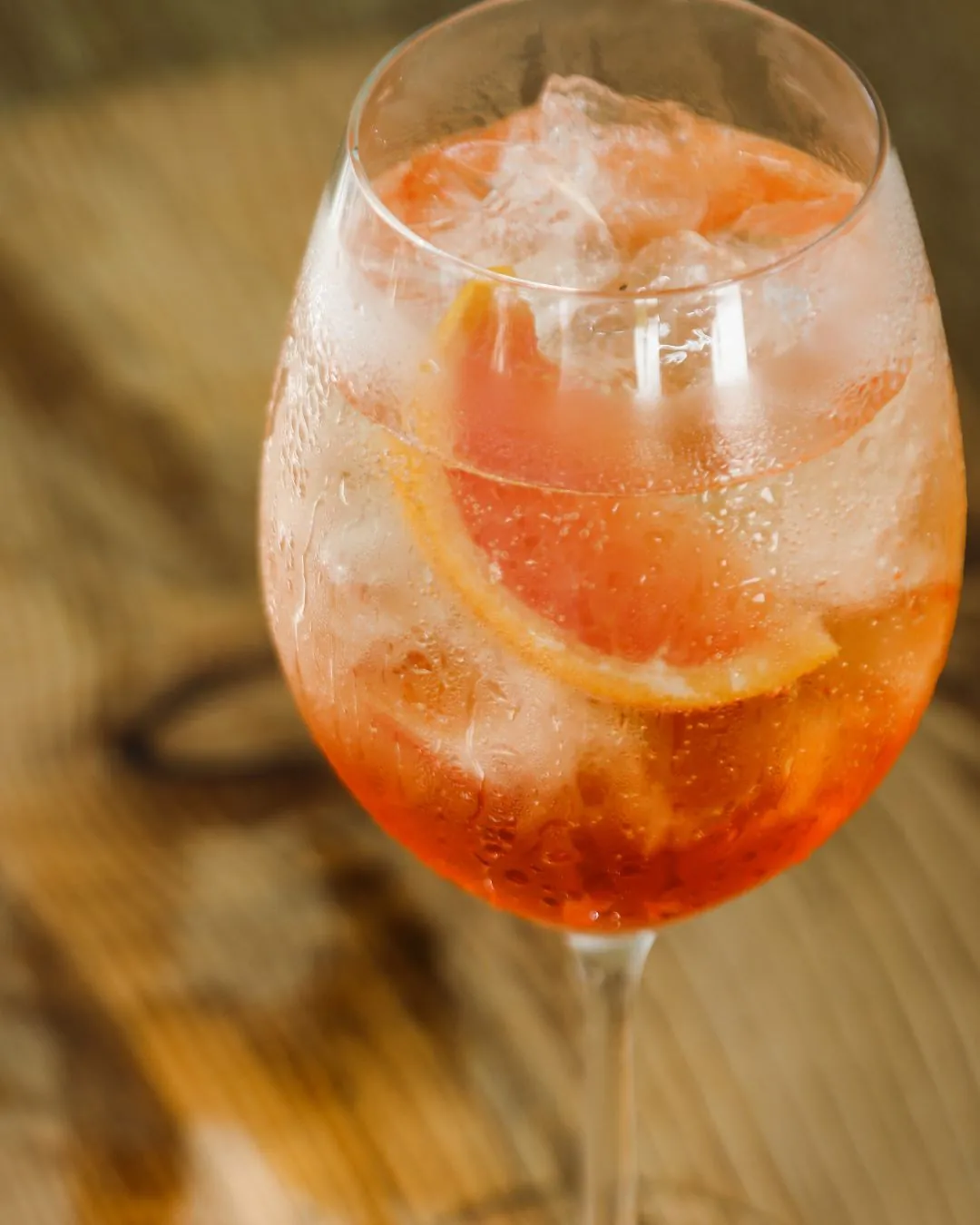 A refreshing grapefruit spritz cocktail served in a stemmed glass with ice and citrus slices, set against a warm wood background.